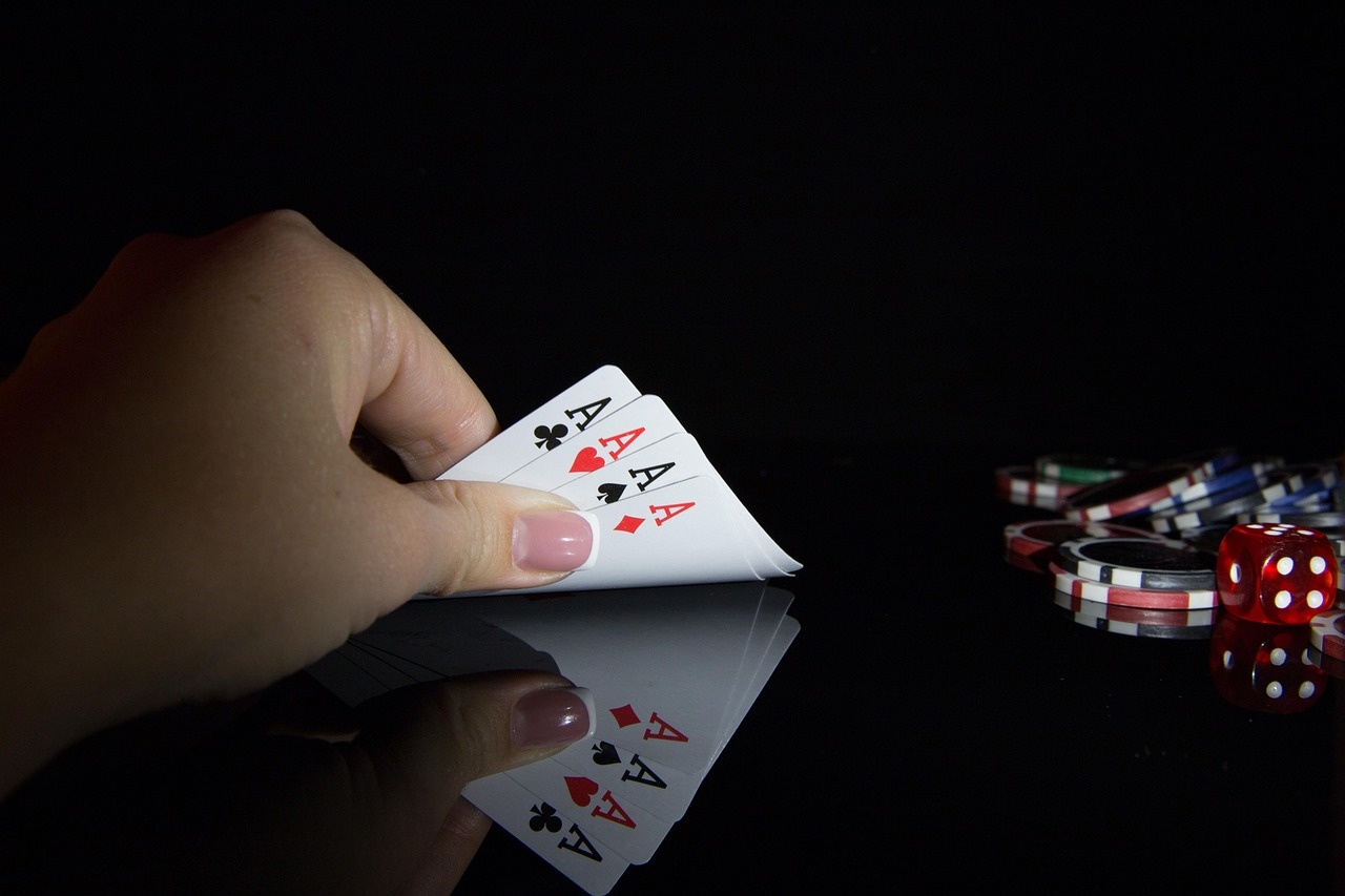 Four aces held above a dark reflective table with chips in the background
