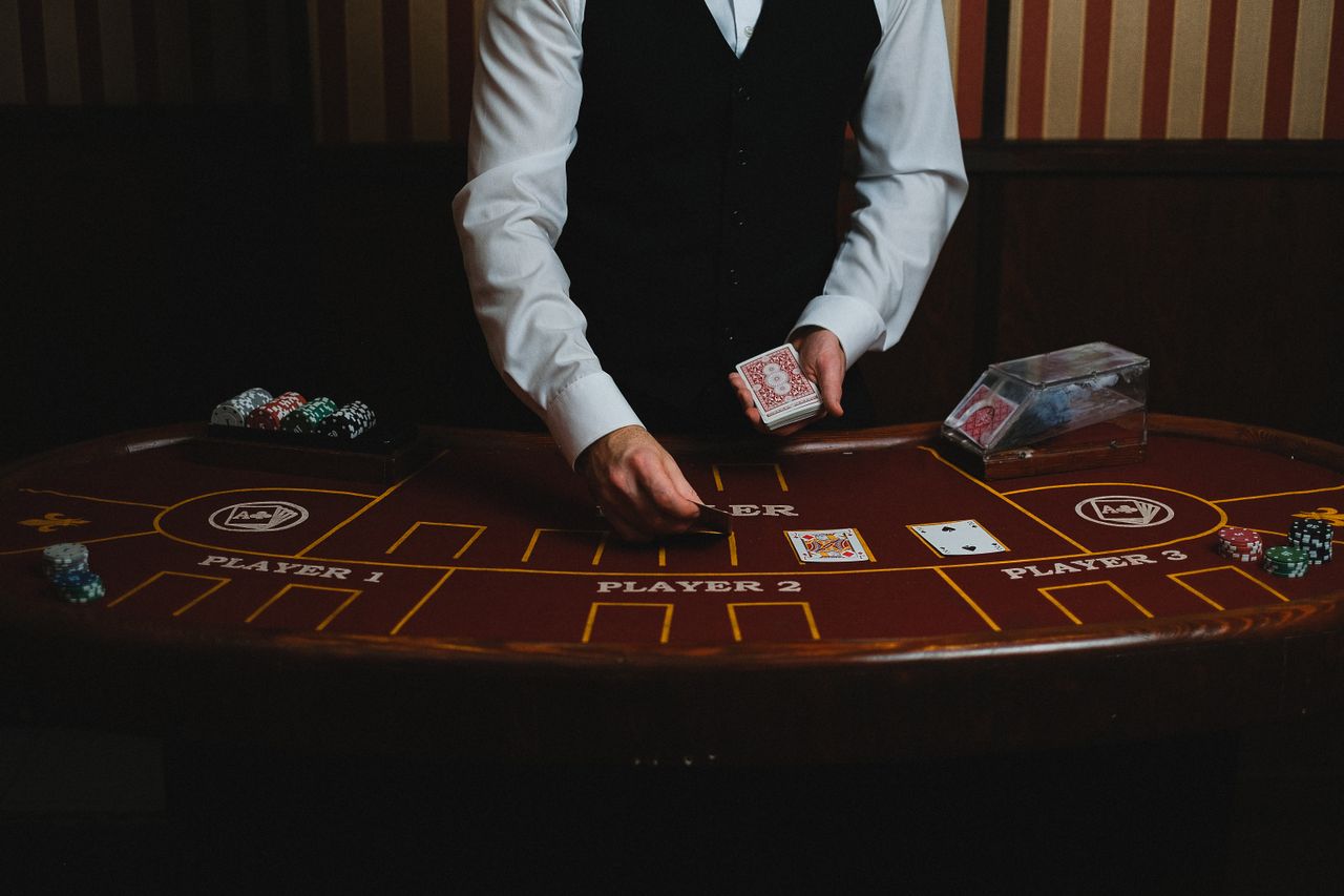 Dealer in evening attire sliding cards across a dark wood gaming table