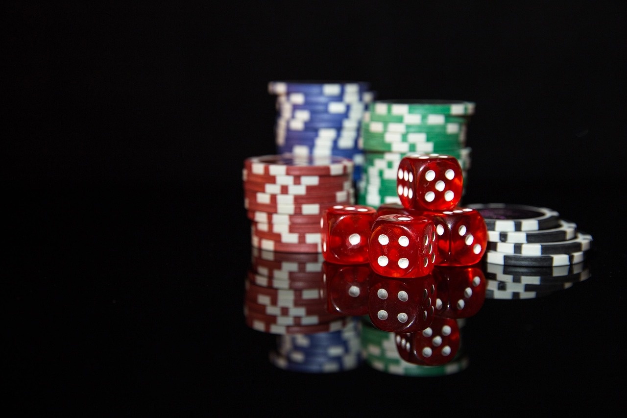 Casino chips and crimson dice arranged on a dark reflective surface