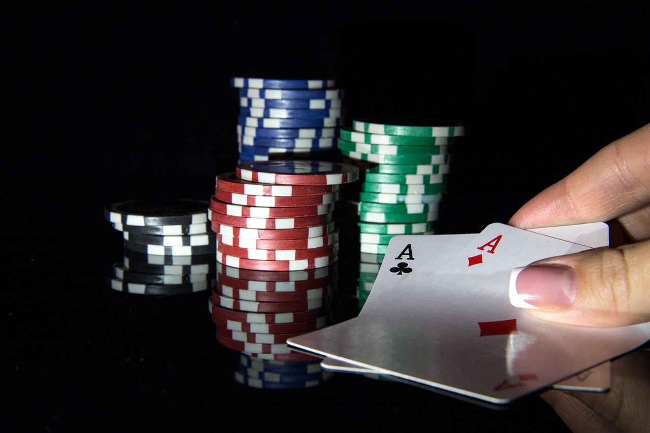 A hand holding the ace of clubs and ace of diamonds beside stacked chips
